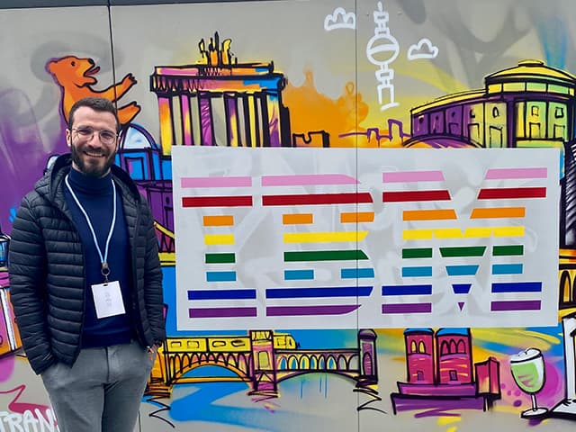 Mann steht neben einer Flagge mit dem IBM Logo in Regenbogenfarben.