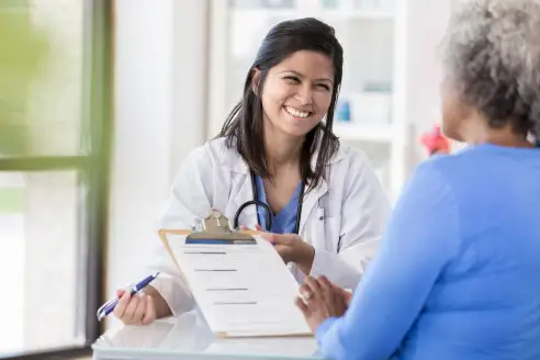 A doctor hands a questionnaire to a patient at the beginning of an appointment.