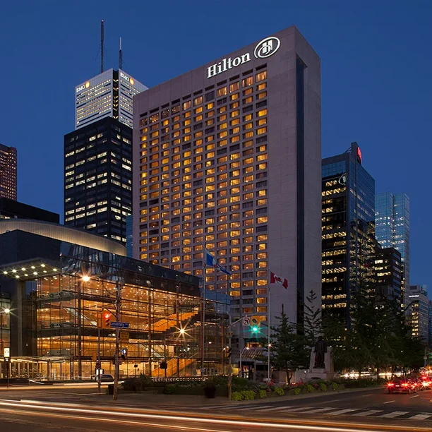 Hilton hotel exterior at dusk in downtown Toronto with illuminated glass entrance and lit city skyscrapers behind