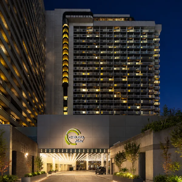 Chelsea Hotel exterior at night, illuminated high-rise tower with glowing windows and lit entrance sign.
