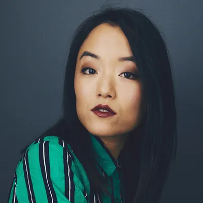 Portrait of a woman with dark hair wearing an emerald green striped blouse against a dark background