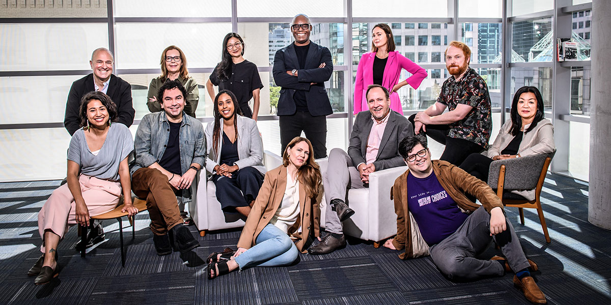 A diverse group of professional film programmers posing together in a modern office space with natural lighting and city views