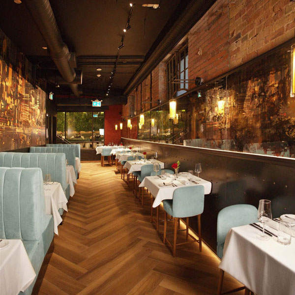 Upscale restaurant interior with herringbone wood floors, mint chairs, and exposed brick walls lit by warm sconces