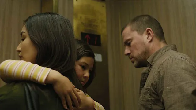 A woman hugs a young girl in an elevator while a somber man stands nearby, all looking downward.