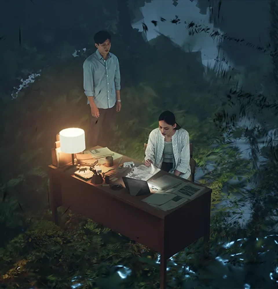 Two people at a lamp-lit desk with a laptop outdoors at night, surrounded by dark forest greenery.