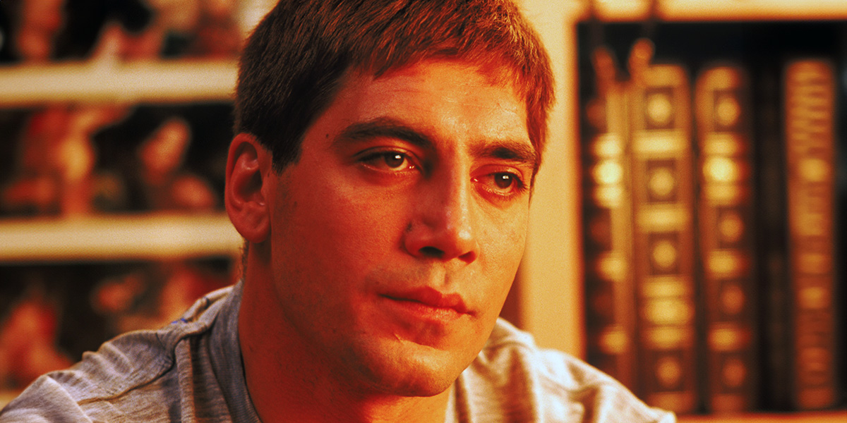 A man in a blue and red stripe polo is sitting amongst some book shelves in a room bathed in orange light