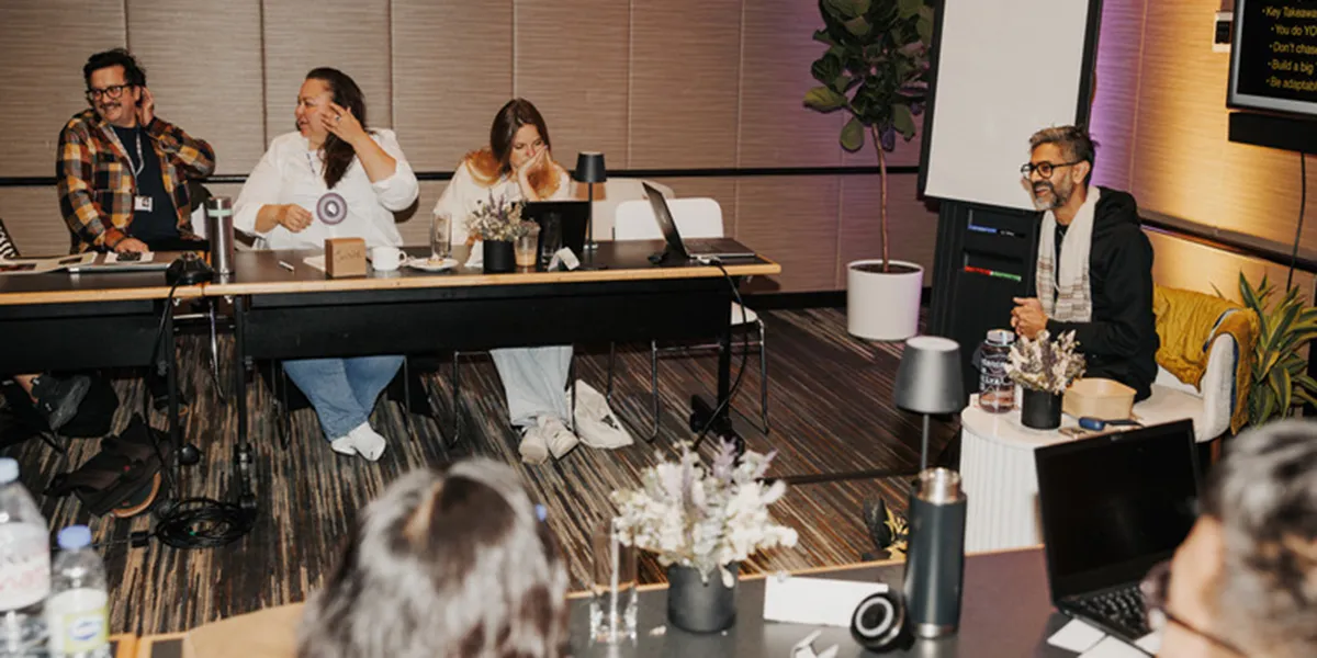A group sharing laughs during a casual business meeting in a modern office space with plants and warm lighting
