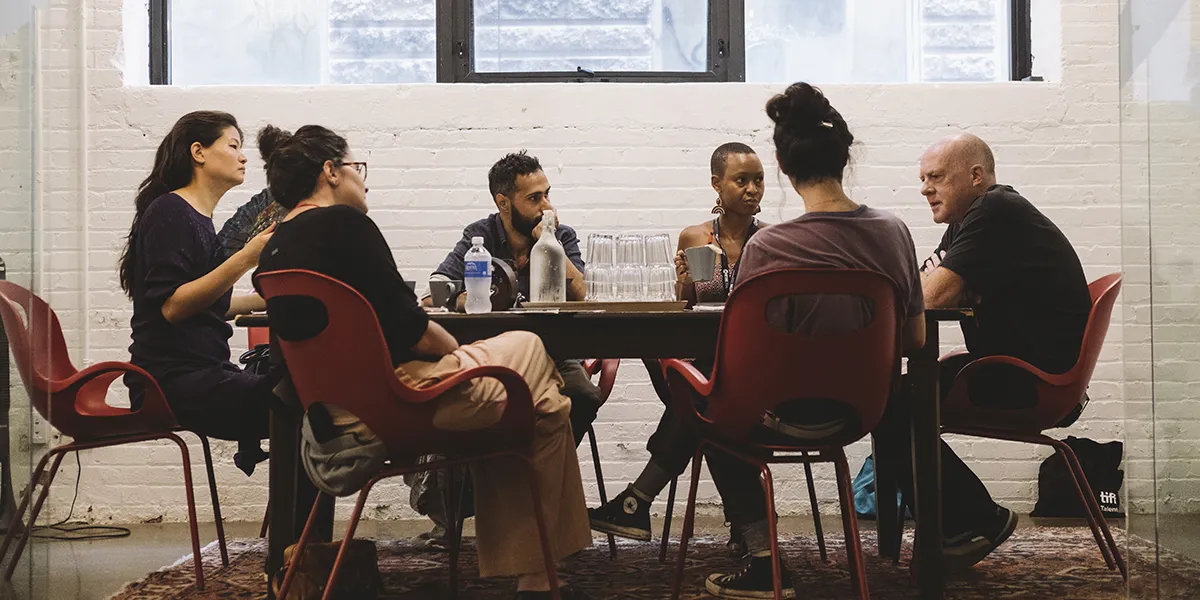 Diverse group of people seated at tables engaged in conversation in a bright room with white brick walls