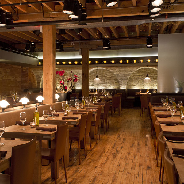 Elegant restaurant interior with exposed brick walls, wooden beams, and warm lighting over set dining tables