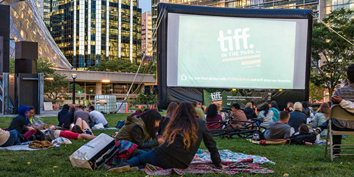 A crowd of people laying and siting on blankets in a park in front of an outdoor movie screen