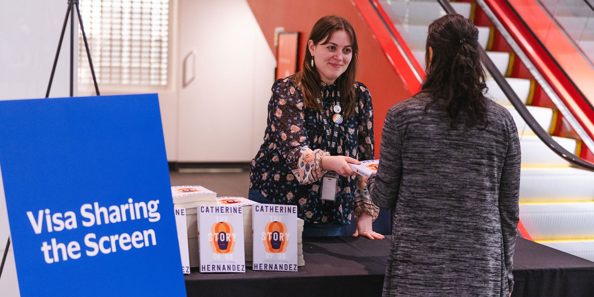 A large group of people holding up the Catherine Hernandez's book, The Story of Us