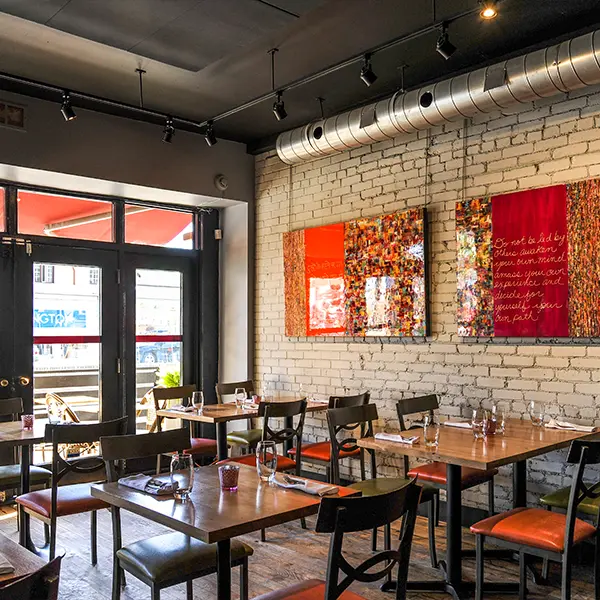 Modern restaurant interior with white brick walls, red artwork, and wooden tables with black chairs