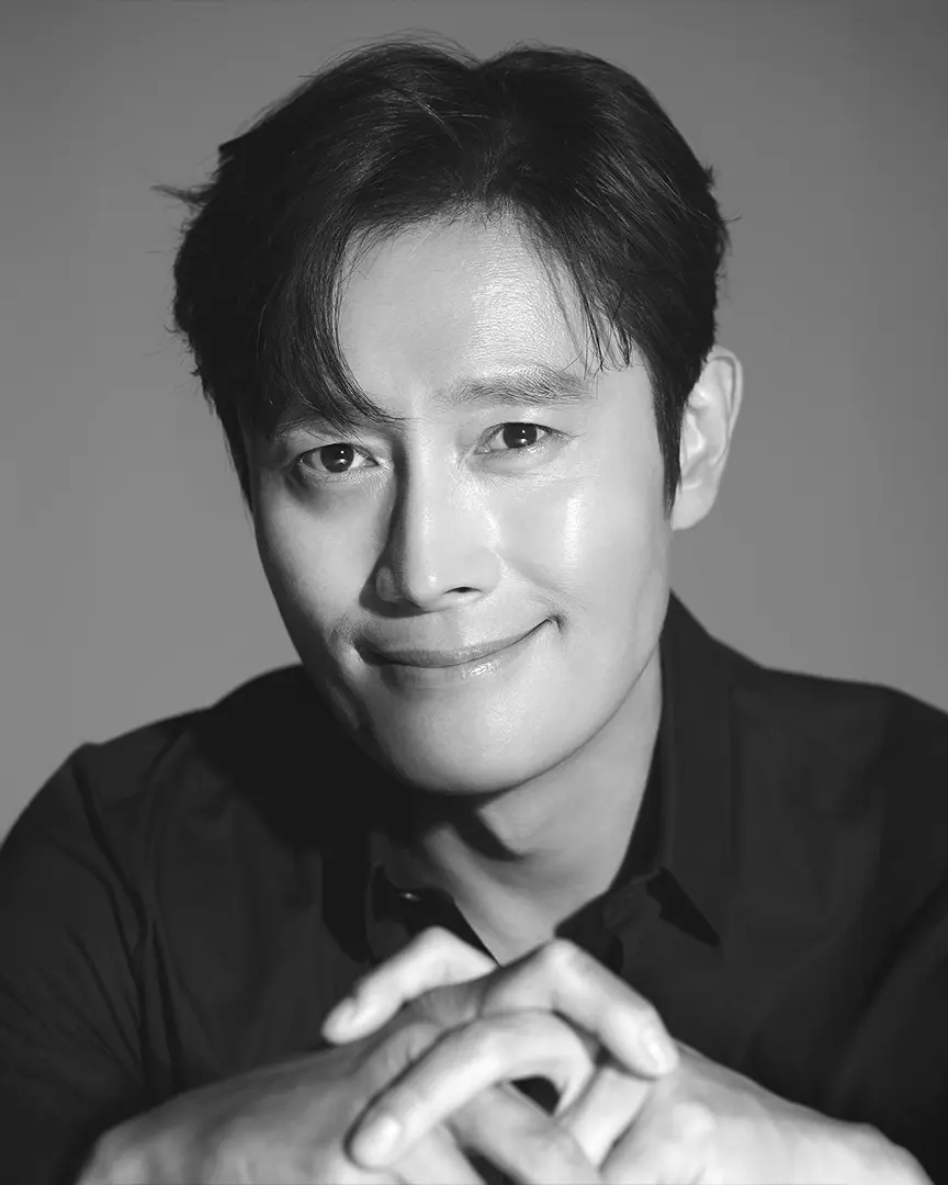 Black and white portrait of Lee Byung-hun in dark clothing with a gentle smile