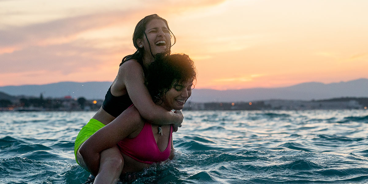 Film still from The Swimmers where two young sisters are laughing and having fun in the water