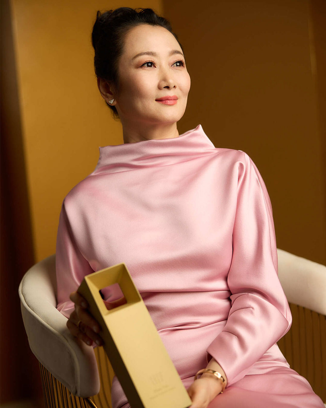 Portrait of Zhao Tao in a pink dress sitting in a chair and holding her award