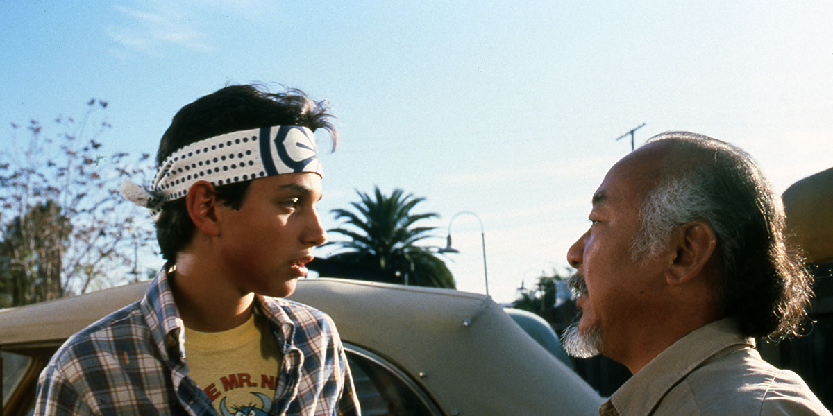 Ralph Macchio and Pat Morita talking ot one another outside a car