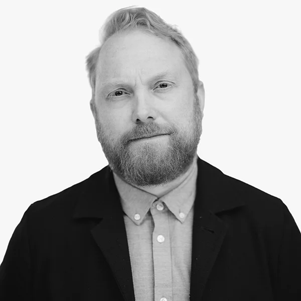 Black and white headshot of a bearded man in a dark blazer and collared shirt.