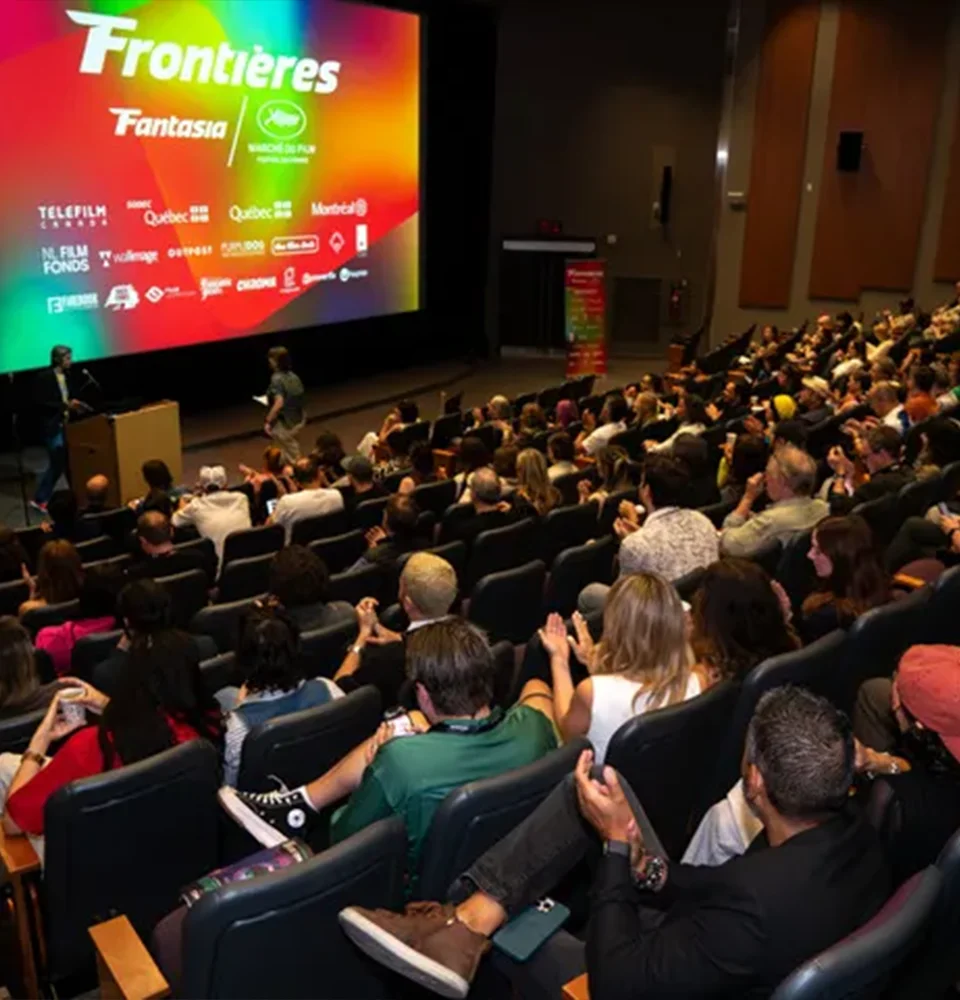 A packed cinema audience faces a colorful screen displaying the Frontières Fantasia film market event.