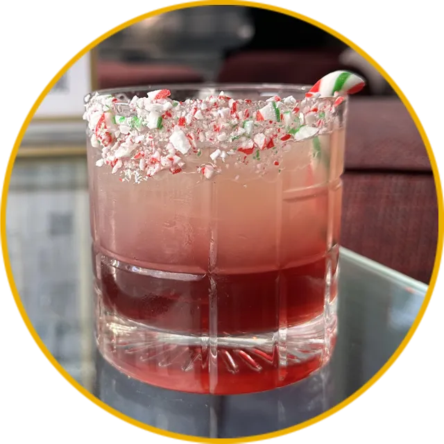 Pink cocktail in glass with crushed peppermint candy rim and festive holiday garnish