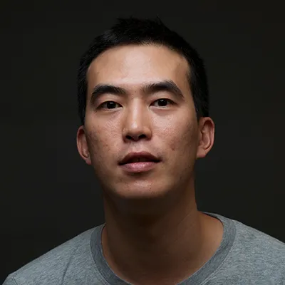 A young Asian man in a grey t-shirt against a dark background