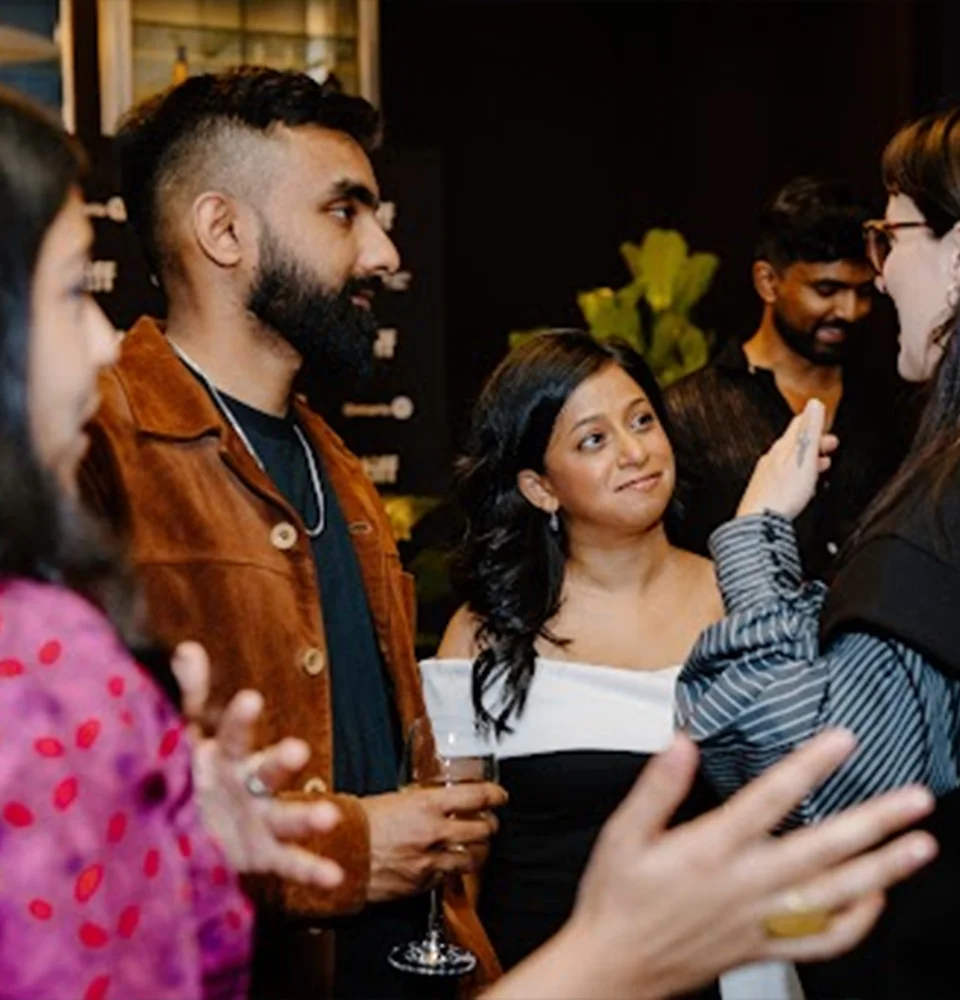 A group of people socializing at an indoor event, holding drinks and engaged in conversation.