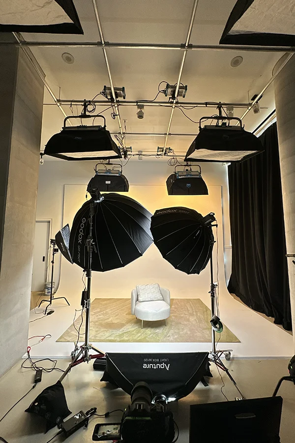 A professional photo studio with multiple Godox and Aputure lights, softboxes, and a white chair on a backdrop.