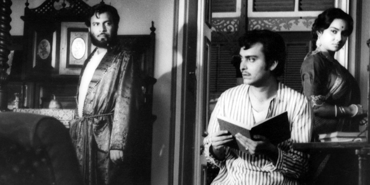 Film still a man looking up from a book with another man and lady in the back of the room from Charulata