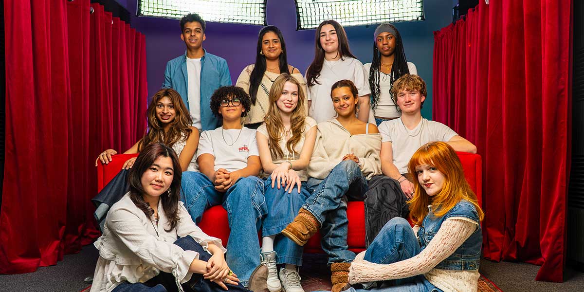 Diverse group of young people posed against red curtain backdrop in casual attire