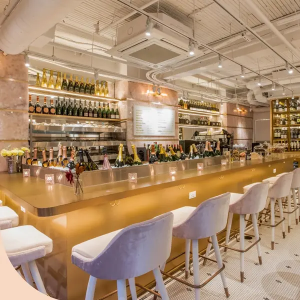Modern bar interior with gold counter, white stools, and illuminated shelves of wine and liquor bottles