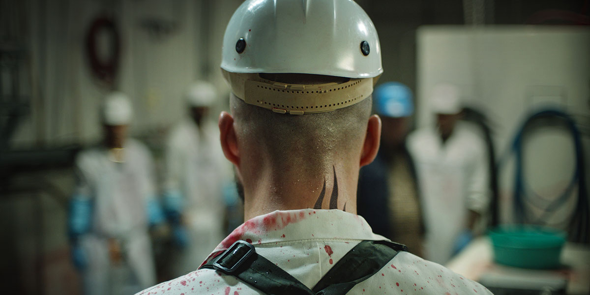 A shot from behind a man in a white safety helmet and clean attire facing a bunch of men also in white cleaning attire