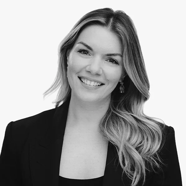 Black and white professional headshot of a smiling woman with long wavy hair wearing a black blazer.