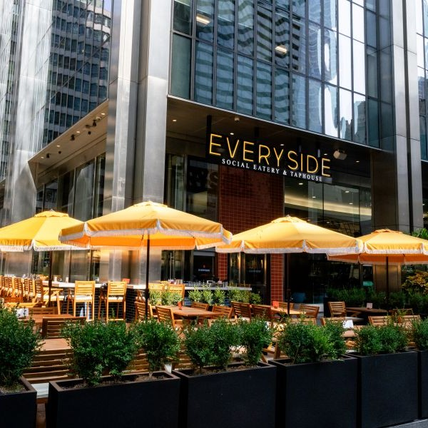 The outdoor patio of Everyside Social Eatery & Taphouse, featuring several bright yellow umbrellas over wooden tables and chairs.