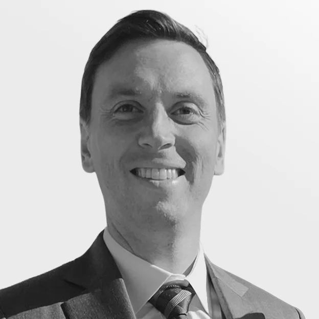 Professional headshot of Matthew MacDonald in a grey suit and a purple tie, smiling warmly against a white background