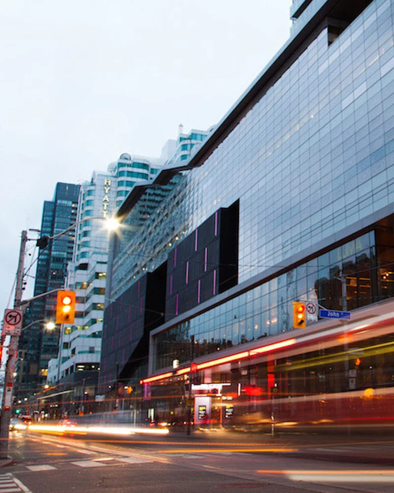Toronto city street at dusk with a glass building, Hyatt hotel, traffic lights, and a blurred red streetcar.
