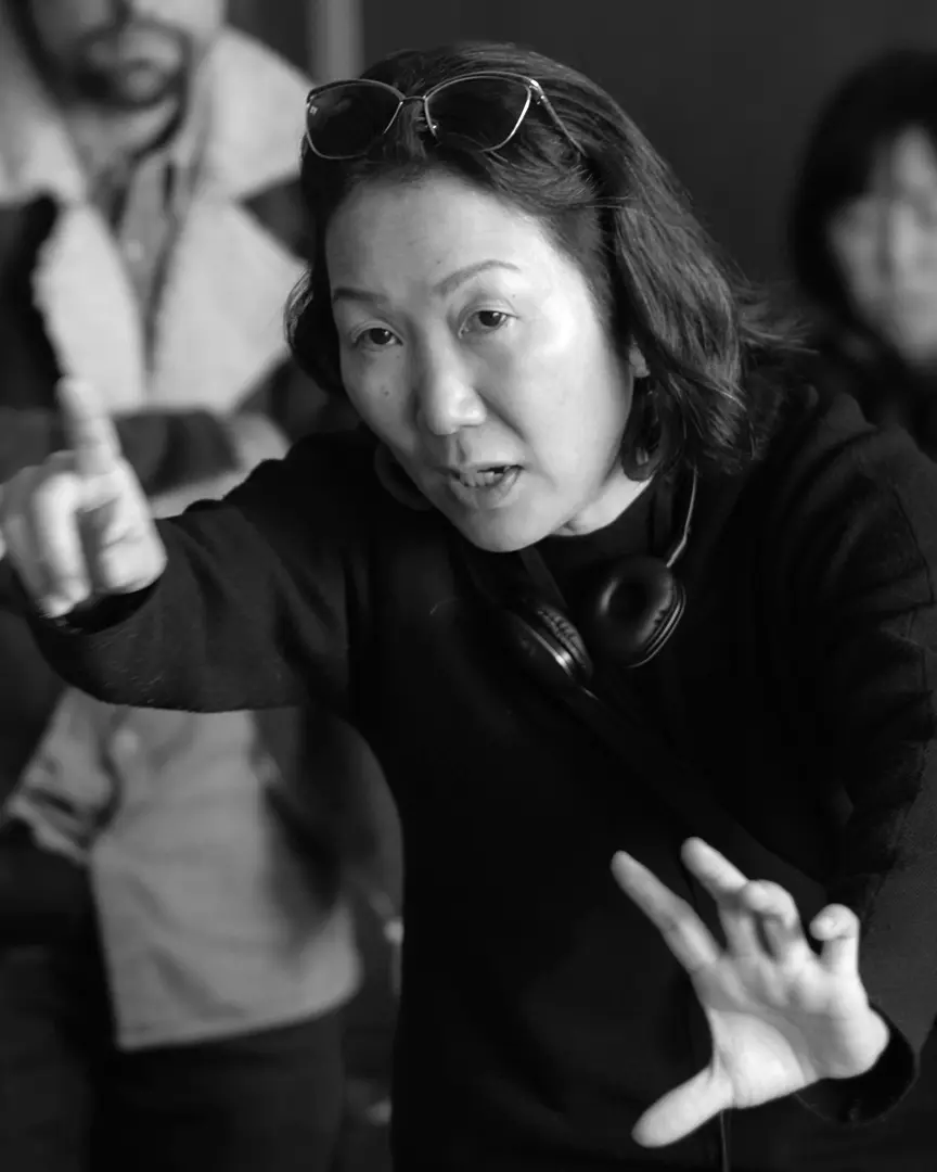 HIKARI in black attire gestures expressively while wearing headphones in a black and white photo
