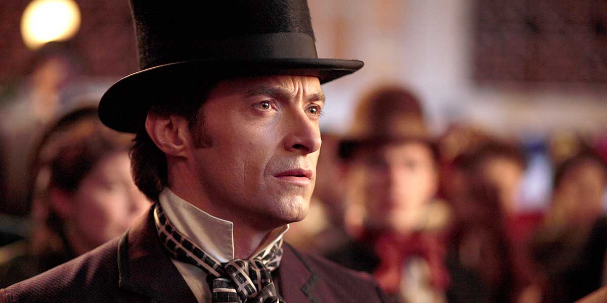 A man in a black top hat and Victorian-era attire gazes seriously amid a blurred crowd.