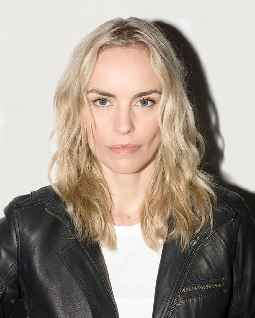 Close-up portrait of a person with wavy blonde hair wearing a black leather jacket and white top