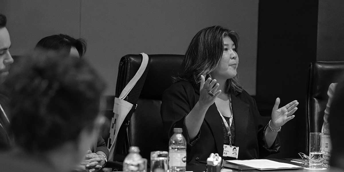 Professional in dark business attire gestures while speaking during a meeting in dimly lit conference room