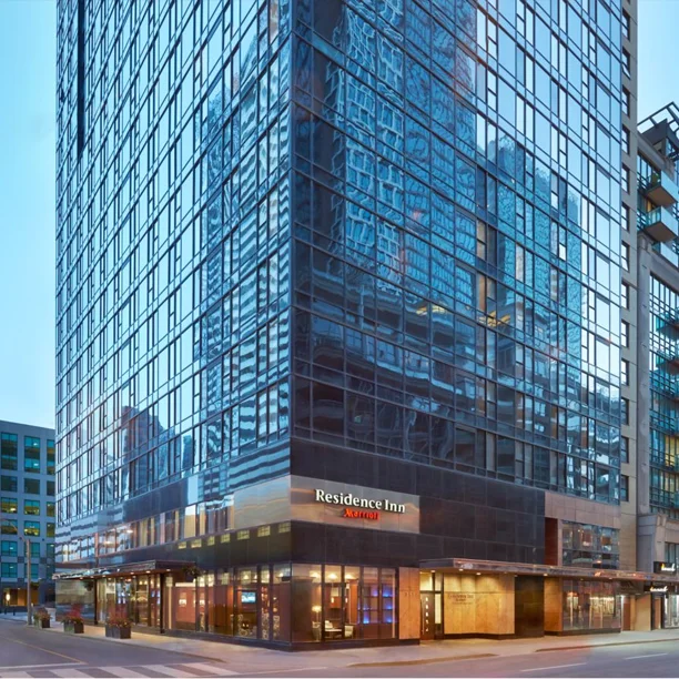 Modern glass high-rise Residence Inn hotel building at dusk with illuminated street-level entrance and retail spaces