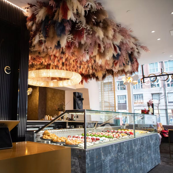 Elegant pastry display case under a dramatic ceiling covered in colourful feathers anda  crystal chandelier