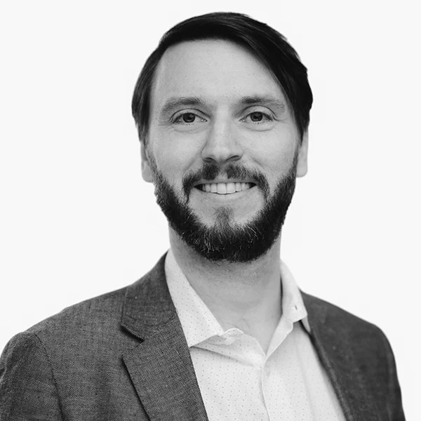 Black and white headshot of a smiling man with a beard, wearing a blazer and collared shirt.