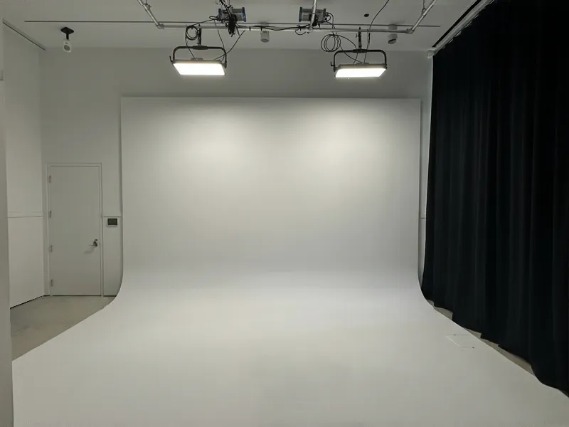Empty photography studio with a white seamless backdrop, ceiling-mounted lights, and a black curtain.