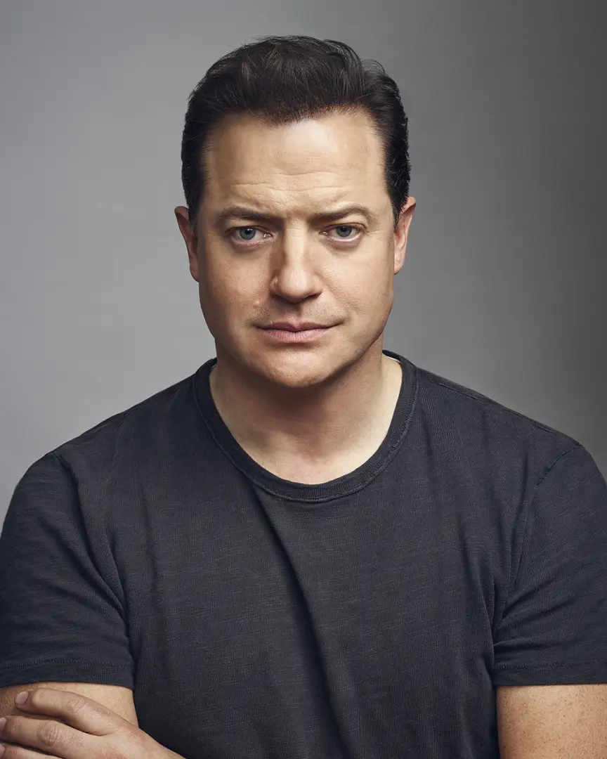 Professional headshot of Brendan Fraser wearing a black t-shirt against a grey background