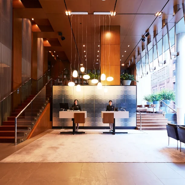Modern hotel lobby with glass walls, pendant lights, and metal reception desks staffed by a concierge team
