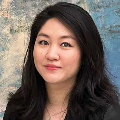 Close-up portrait of a woman against a textured blue wall background, featuring long black hair and a warm smile