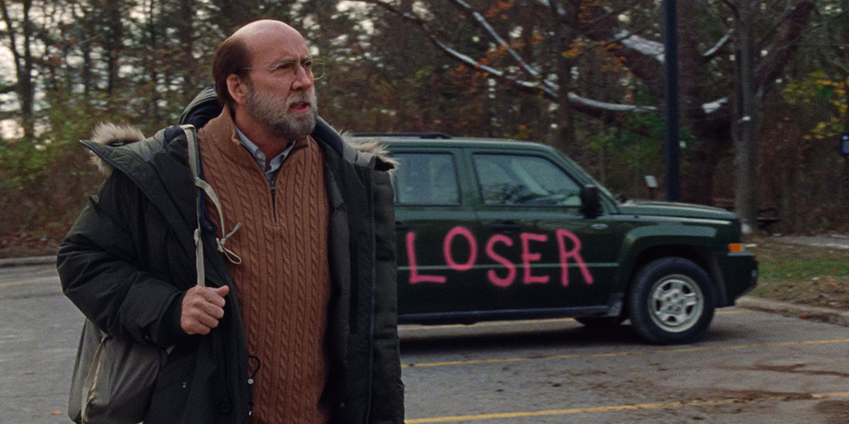 Nicolas Cage as an inconspicuous academic standing in front of an SUV with LOSER graffiti on it, in the film Dream Scenario