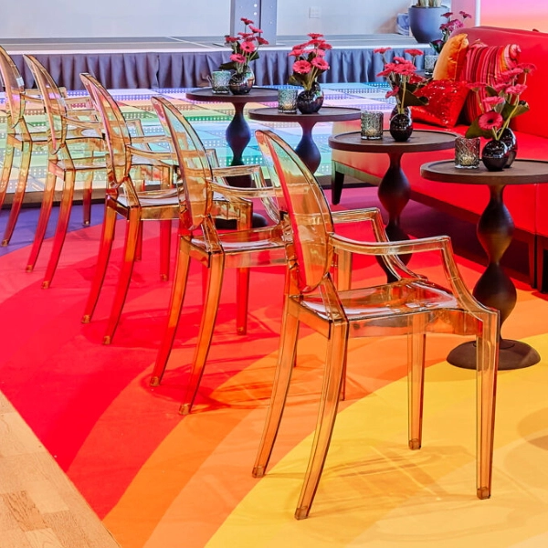 A colorful lounge area with clear acrylic armchairs, small side tables, and a bright red sofa in the background.