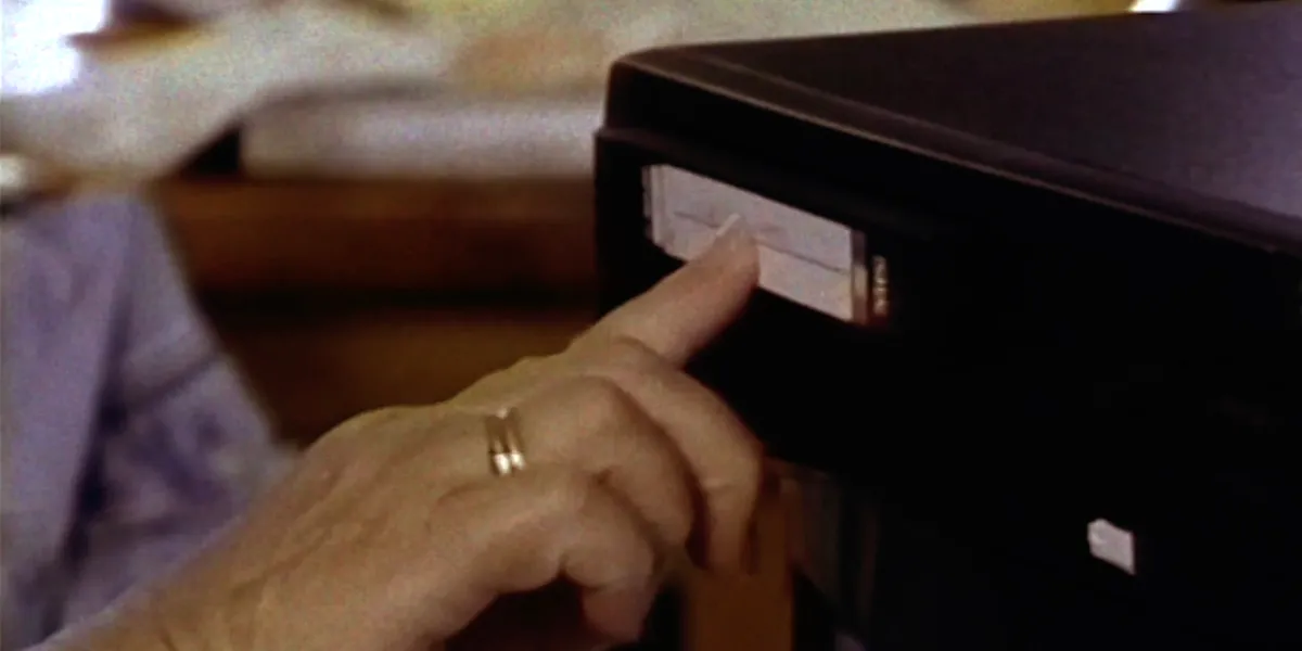 Hand inserting a VHS tape into a black VCR player
