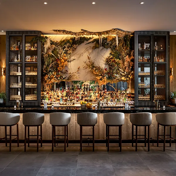 Elegant bar interior with dried floral decor, glass cabinets of spirits, and row of black barstools