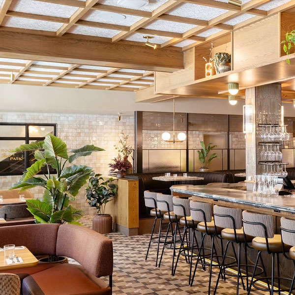 Modern restaurant interior with bar seating, exposed wood beams, and large tropical plants